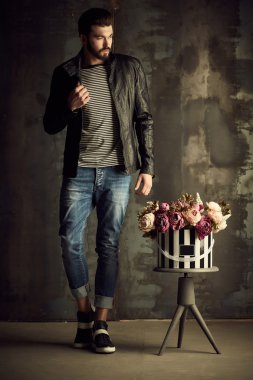 Yakışıklı delikanlı buket çiçek ile akıllı ceketli duvarın önünde poz veriyor.