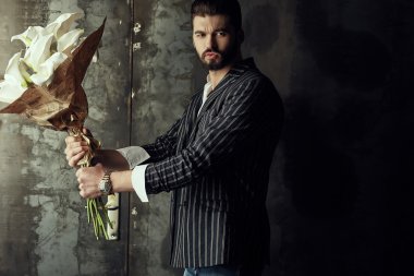 Yakışıklı delikanlı buket çiçek ile akıllı ceketli duvarın önünde poz veriyor.