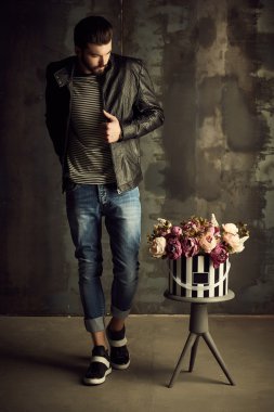 Yakışıklı delikanlı buket çiçek ile akıllı ceketli duvarın önünde poz veriyor.