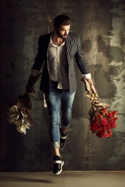 Yakışıklı delikanlı buket çiçek ile akıllı ceketli duvarın önünde poz veriyor.