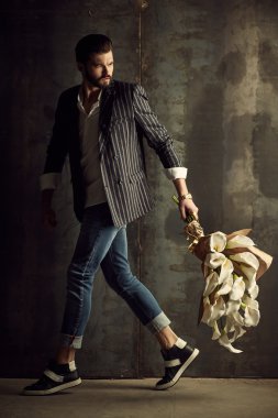 Yakışıklı delikanlı buket çiçek ile akıllı ceketli duvarın önünde poz veriyor.