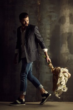 Yakışıklı delikanlı buket çiçek ile akıllı ceketli duvarın önünde poz veriyor.