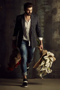 Yakışıklı delikanlı buket çiçek ile akıllı ceketli duvarın önünde poz veriyor.