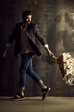 Yakışıklı delikanlı buket çiçek ile akıllı ceketli duvarın önünde poz veriyor.