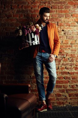 Yakışıklı delikanlı buket çiçek ile akıllı ceketli duvarın önünde poz veriyor.