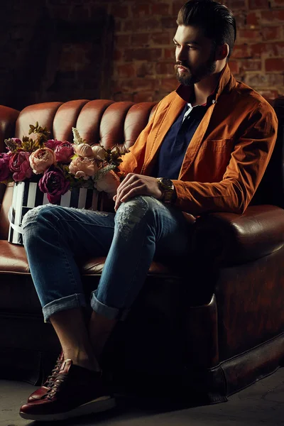 Bello giovanotto in giacca intelligente con mazzo di fiori posa davanti al muro — Foto Stock