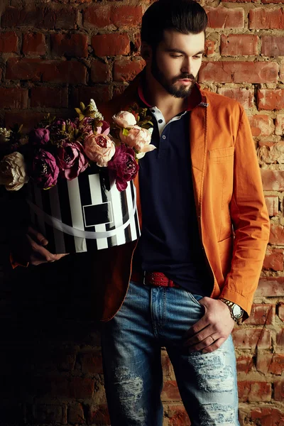 Handsome young man in smart jacket with bouquet of flowers  poses in front of the  wall