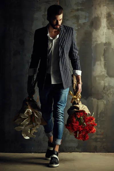 Csinos, fiatal férfi az intelligens kabát csokor virágot jelent, a fal előtt — Stock Fotó