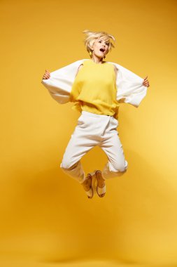 Genç kız eğleniyor ve atlama. Moda giyim eşyası sarı arka plan ile gülümseyen kız