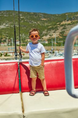 Komik küçük çocuk güzel dağlar yakınındaki gezi teknesinde poz