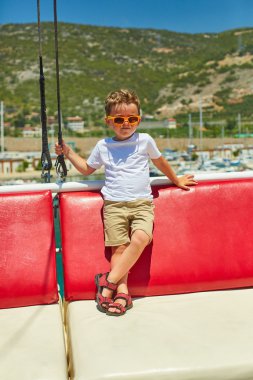 Komik küçük çocuk güzel dağlar yakınındaki gezi teknesinde poz