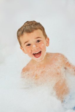 Happy little boy playing in foam bath clipart