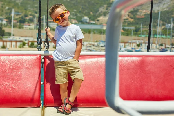 Engraçado menino posando em barco de excursão perto de belas montanhas — Fotografia de Stock