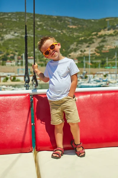 Engraçado menino posando em barco de excursão perto de belas montanhas — Fotografia de Stock