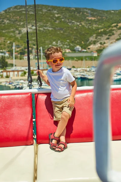 Engraçado menino posando em barco de excursão perto de belas montanhas — Fotografia de Stock