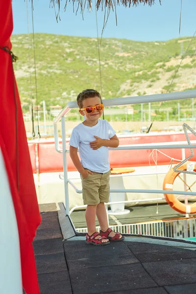 Engraçado menino posando em barco de excursão perto de belas montanhas — Fotografia de Stock