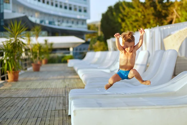 Menino bonito pulando perto de espreguiçadeiras na zona de natação — Fotografia de Stock
