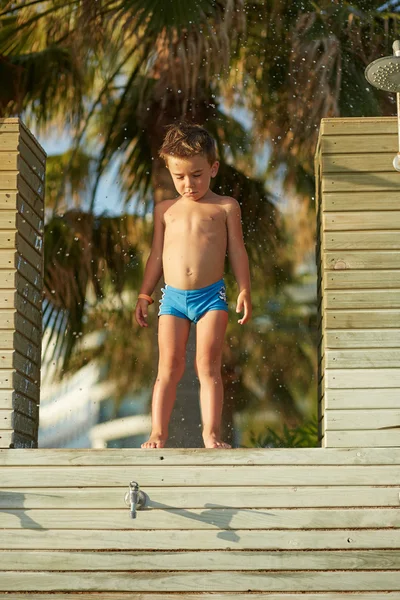 Menino bonito em calções de banho posando sob a palma da mão — Fotografia de Stock