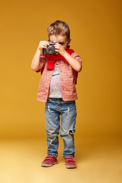 Lindo niño con cámara en estudio con fondo amarillo — Foto de Stock