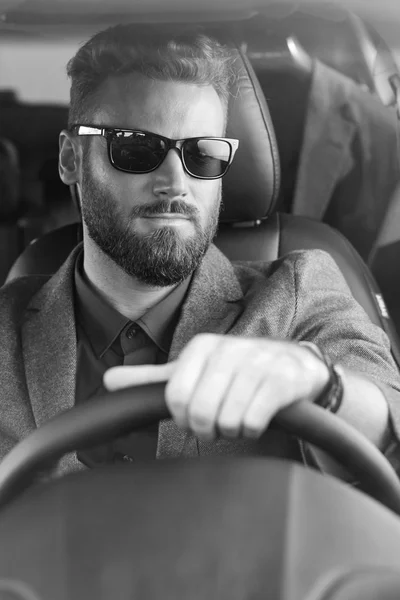 Привлекательный серьезный мужчина в черных очках водит машину в черно-белом — стоковое фото