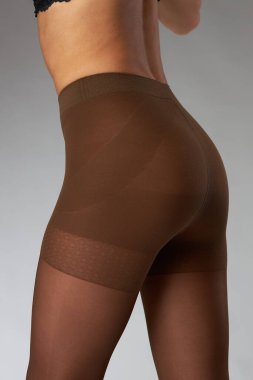 Stüdyoda gri arka planda bir model üzerinde naylon tayt reklamı çekimi yapıyor. Kahverengi tayt giyiyor. 