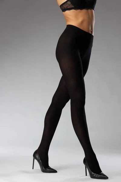 advertising shooting of nylon tights on a model in the studio on a gray background, she is wearing black tights and black heels