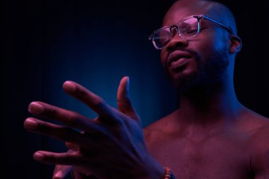 Gözlerinde gözlük, kollarında bilezik ve kollarında çıplak spor gövdesi olan, koyu renk arka planda mavi ve kırmızı renkli yakışıklı bir adamın duygusal portresi.