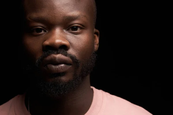 portrait of a dark-skinned handsome guy on dark background in pink sweater stands with serious face and looks in camera