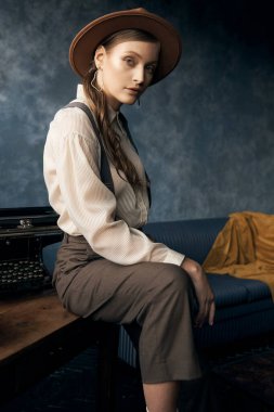 Eski tarz bir kızın portre fotoğrafı. İç stüdyoda poz veriyor. Pantolon, gömlek, pantolon askısı ve şapka giyiyor.