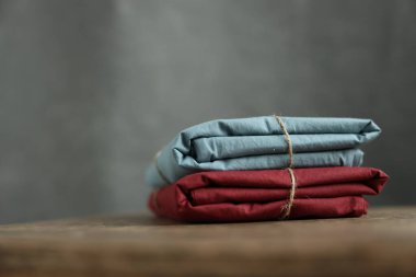 Bordo ve turkuaz renklerle yıkanmış 2 doğal ve ekolojik pamuk kumaşın fotoğrafı üzerinde çuval ipliği ve yeşil bitkiyle geri sarılmış.