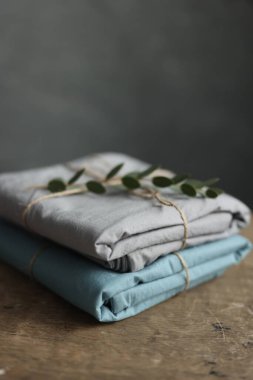 2 doğal ve ekolojik kumaşın gri ve turkuaz renklerle yıkanmış fotoğrafı üzerinde çuval ipliği ve yeşil bitkiyle geri sarılmış.
