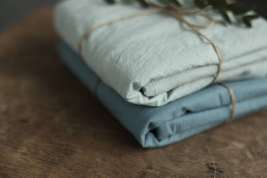 Nane ve turkuaz renklerle yıkanmış 2 doğal ve ekolojik pamuk kumaşın fotoğrafı üzerinde çuval ipliği ve yeşil bitki ile geri sarılmış.