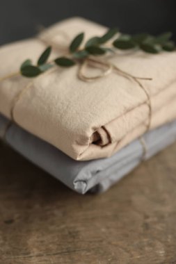 2 doğal ve ekolojik kumaşın bej ve gri renklerle yıkanmış fotoğrafı üzerinde çuval ipliği ve yeşil bitkiyle geri sarılmış.