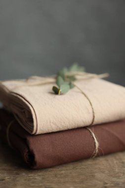 2 doğal ve ekolojik kumaşın bej ve kahverengi renklerle yıkanmış fotoğrafı. Üzerinde çuval iplik ve yeşil bitki ile geri sarılmış.