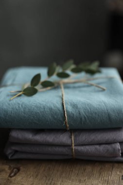 2 doğal ve ekolojik kumaşın gri ve turkuaz renklerle yıkanmış fotoğrafı üzerinde çuval ipliği ve yeşil bitkiyle geri sarılmış.