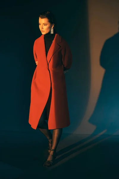 Töprengő Vonzó Lány Piros Hosszú Kabátban Sötét Háttérrel Összehajtott Karokkal — Stock Fotó