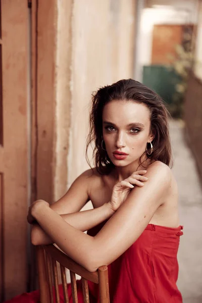 迷人的黑发 穿着红色长裙 相貌漂亮 坐在西班牙一条小街上阳台上的椅子上 涂红的嘴唇 迷人的褐色眼睛 图库图片