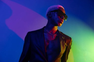 Siyah ceketli koyu tenli adam ve mavi-yeşil ışıkta gümüş mücevher.