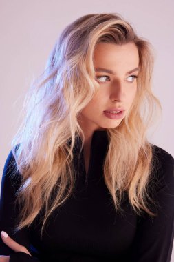 Sarışın, kıvırcık saçlı, yana bakan. Siyah bir kazak giymişti.