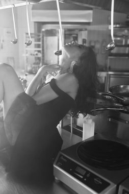 Lokanta mutfağında poz veren siyah kısa elbiseli güzel bir kızın fotoğrafı.