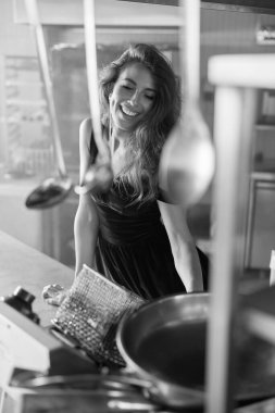 Gülümseyen siyah saçlı, uzun saçlı, gülümseyen ve yüzünü çeviren bir kız. Lokantanın mutfağında siyah beyaz fotoğraf var.