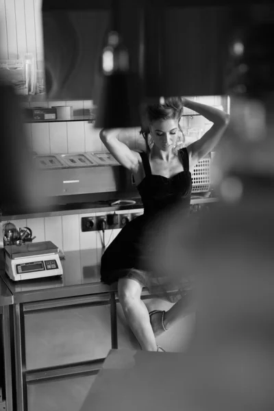 照片上一个女孩坐在厨房的工作面上 黑白照片 那女孩穿着一件黑色的衣服 把头发竖起来 — 图库照片