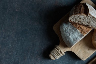 Taze ekmek ve ahşap tahtayla siyah bir zemin üzerinde kompozisyon