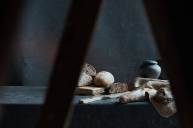 Siyah arka planda yatay natürmort fotoğrafı. Fotoğrafta farklı ekmek türleri ve siyah bir sürahi var.