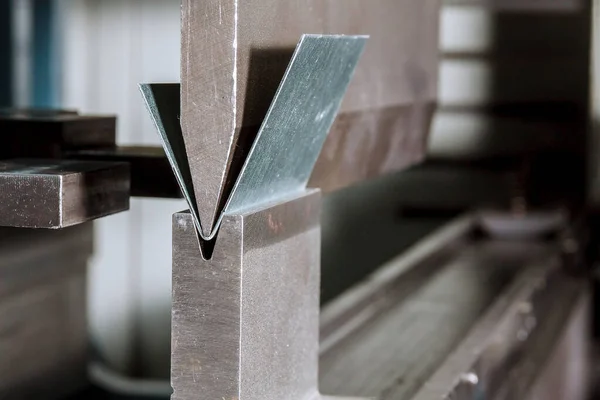 Bending sheet metal on a hydraulic machine at the factory. Bend tools, press brake punch and die. Close-up.