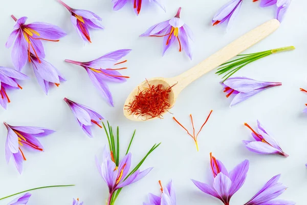 Tahta kaşığın içindeki safran baharatı beyaz arka planda, kır çiçeklerinin arasında. Yemek, kozmetoloji ve geleneksel tıpta kullanılan safran baharatı.