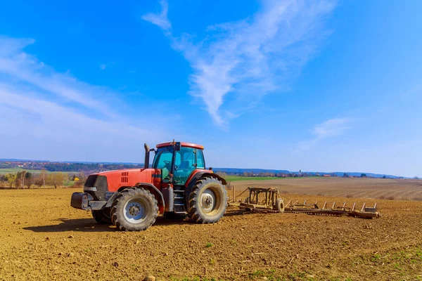 Seorang petani membajak tanah di ladang dengan bajak pahat di atas traktor. Traktor pertanian dengan bajak di lahan pertanian. — Stok Foto