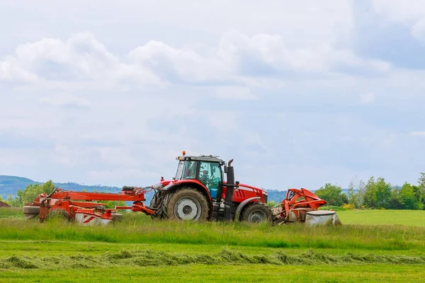 İki çim biçme makineli büyük kırmızı traktör çimleri biçer. — Stok fotoğraf