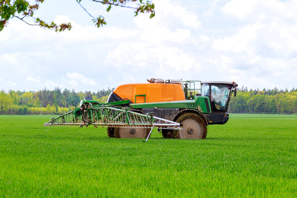 Pesticide spraying of young wheat in the field using a tractor sprayer.