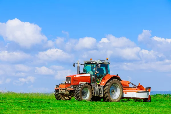 Большой красный трактор с косилкой косит траву на поле в солнечный день — стоковое фото
